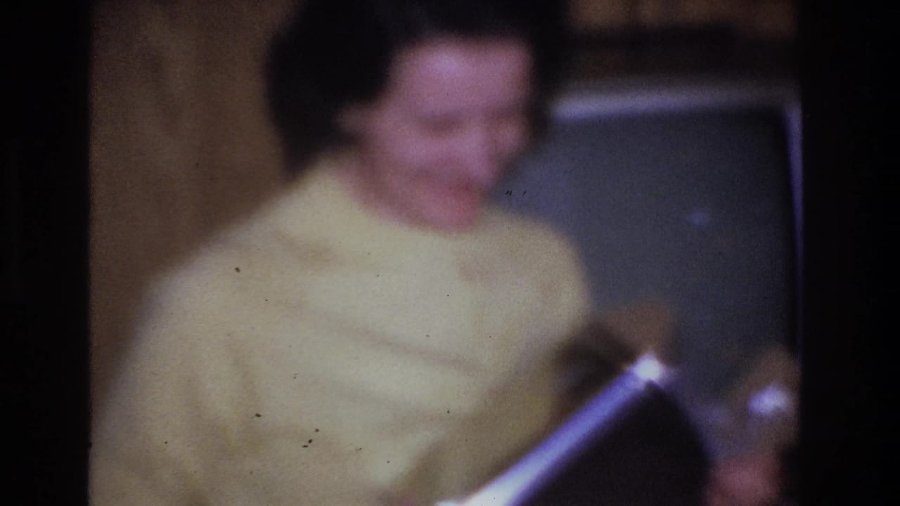 Blurred close-up of a woman in a yellow sweater in what appears to be a mid-1960s American living room; a boxy vintage television is partially visible behind her.