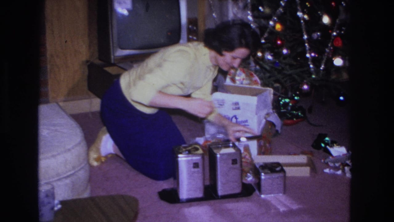 Woman reaches toward gifts and metal canisters beside a decorated Christmas tree.