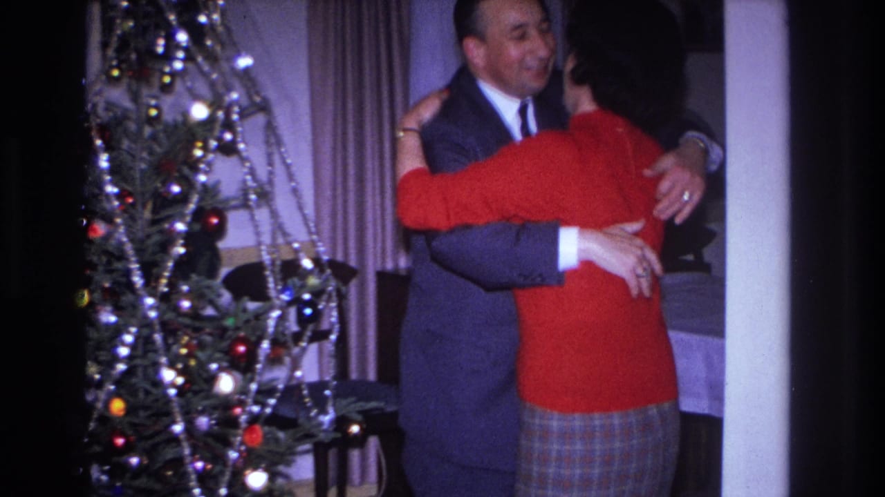 In 1966 Hoboken home-movie footage, a suited man embraces a woman in a red sweater near a Christmas tree.