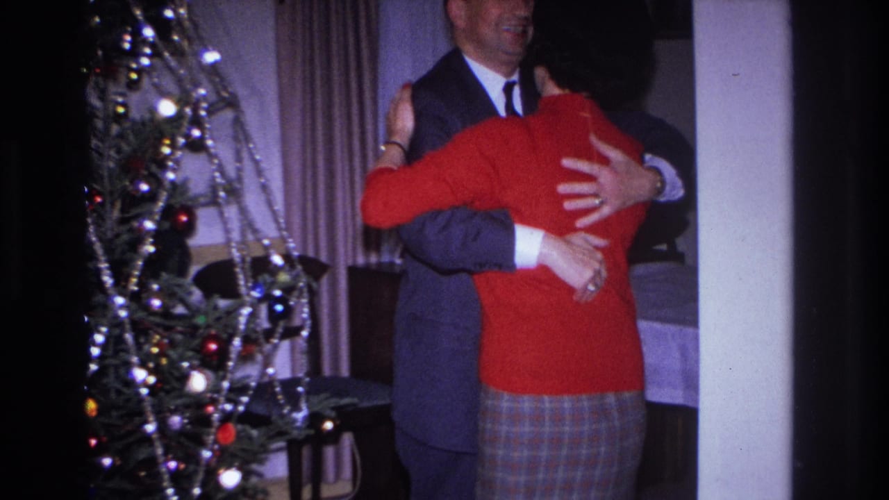 Couple continues embracing beside a Christmas tree, with the woman's back toward the camera.
