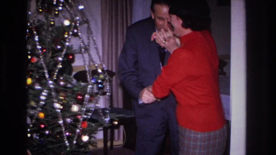Man kissing a woman's hand beside a tinsel-draped Christmas tree in a home interior, Hoboken, New Jersey, circa 1966, on 8mm film.