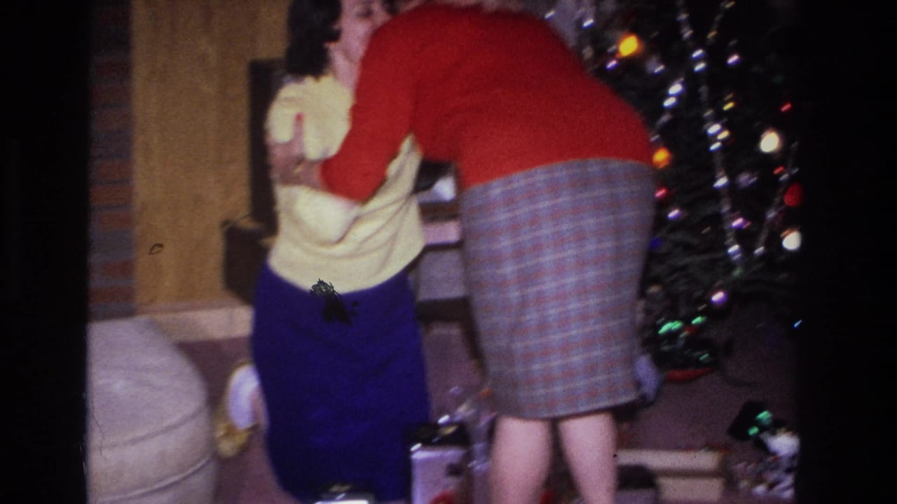 Two women, backs to camera, stand beside a decorated Christmas tree in a living room.