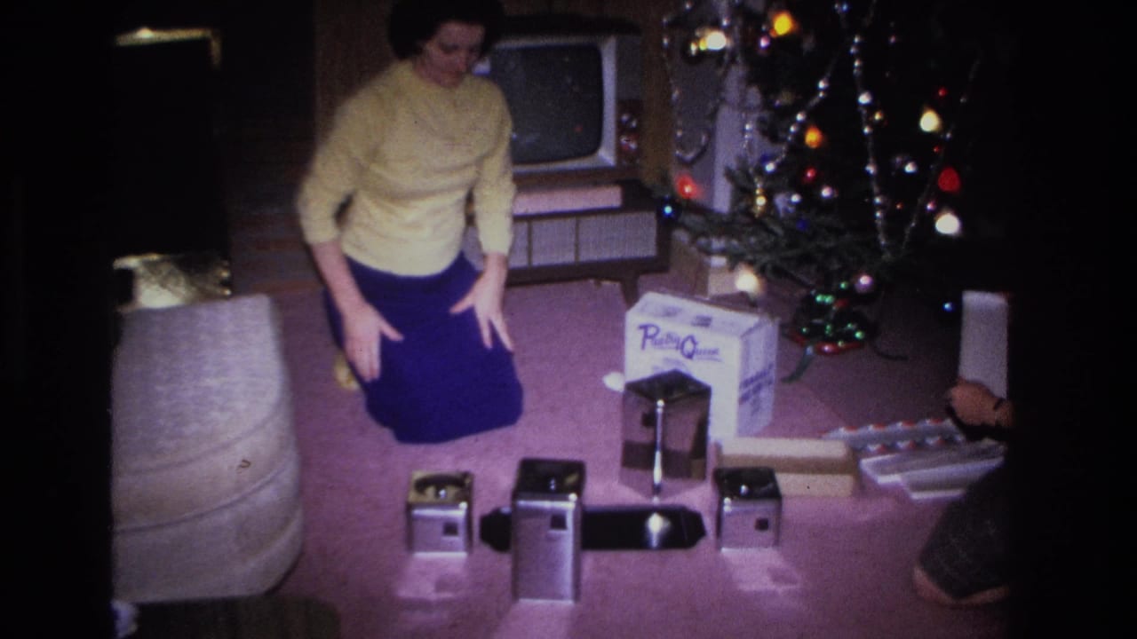 Woman in yellow sweater and blue skirt standing upright near Christmas tree and gifts, with a vintage CRT television visible behind her.