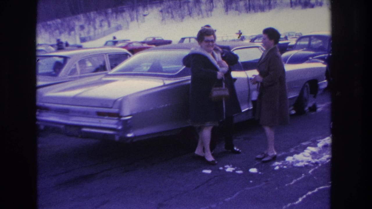 Two women in 1960s winter coats and handbags beside a large mid-decade American sedan in a winter parking lot, Hoboken, New Jersey area, circa 1966.