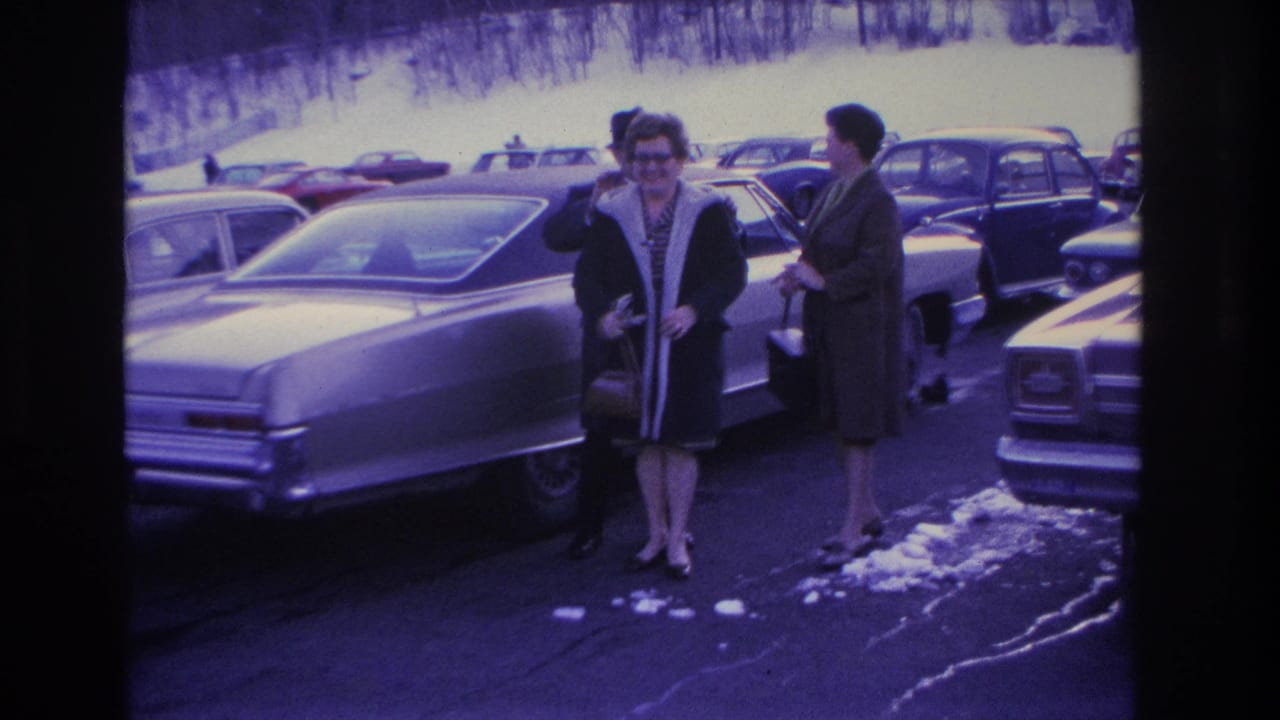 Two women in mid-1960s winter coats — one wearing glasses — near the rear of a large American sedan in a snow-patched parking lot, Hoboken, New Jersey area, circa 1966.