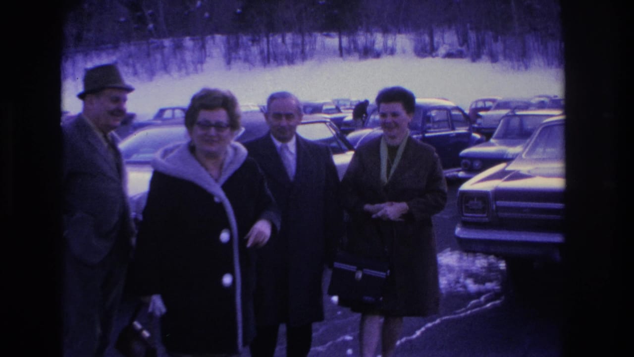 Four adults in 1960s attire, including fedora hats, wool coats, and a fur collar, gather in a parking lot in Hoboken, New Jersey, circa 1966, surrounded by period American sedans.