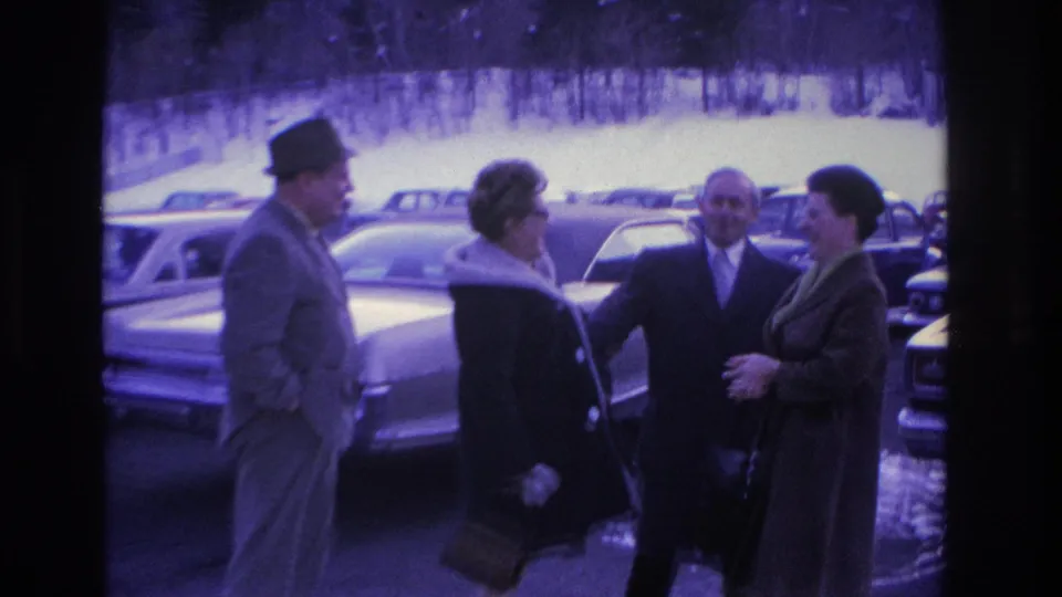 Four adults in mid-1960s winter attire, fedoras and fur-collar coats, greeting in a busy parking lot; dated circa 1966, Hoboken, New Jersey per metadata.