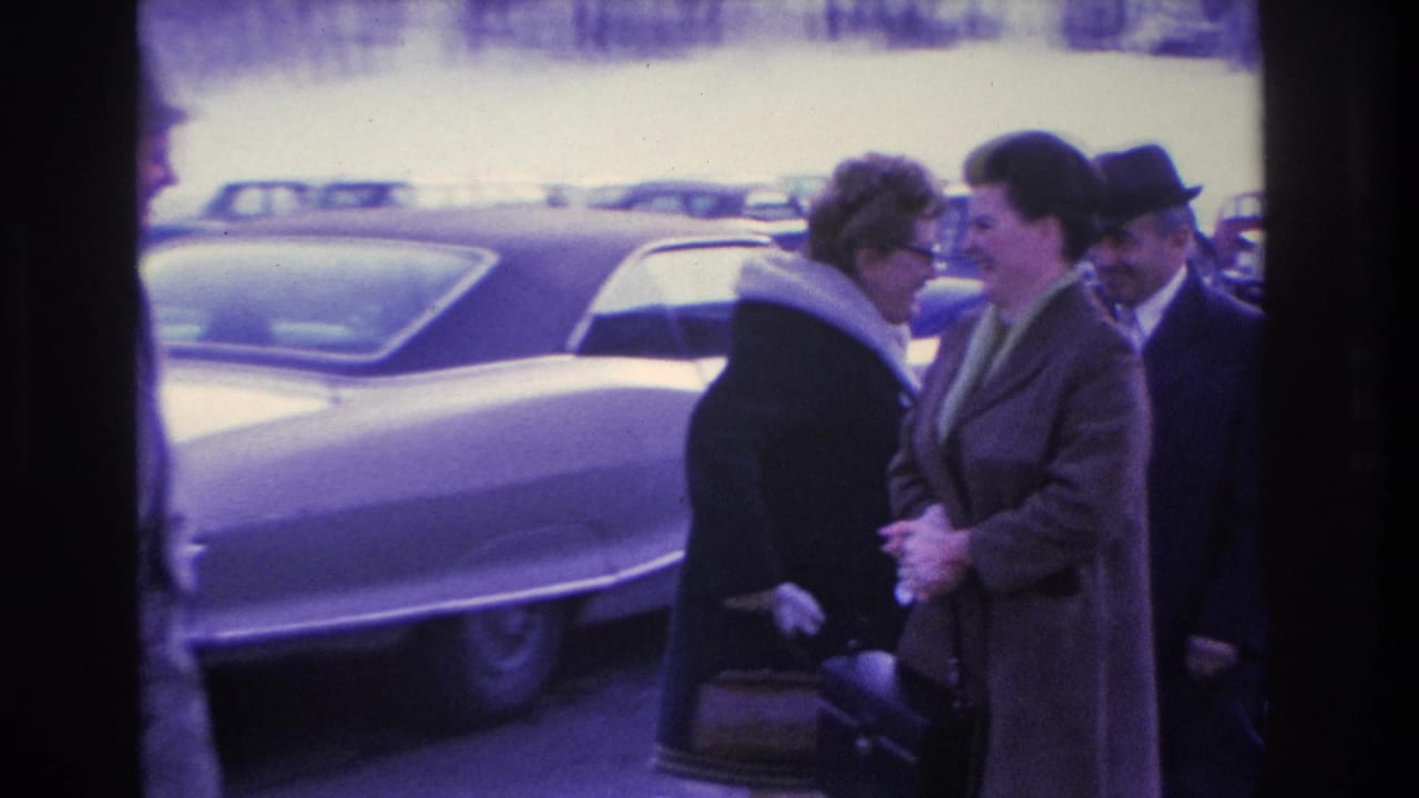 Close shot of two women and a man in 1960s winter dress beside the hood of a large mid-century American car; circa 1966, Hoboken, New Jersey per metadata.