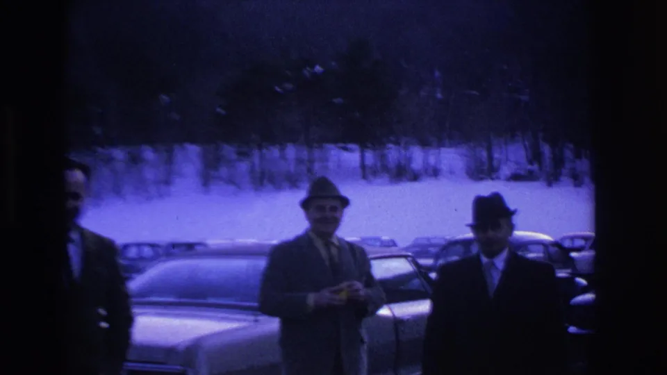 Three men in suits and fedoras stand in a snowy parking lot, Hoboken New Jersey area circa 1966, with classic American sedans visible behind them.