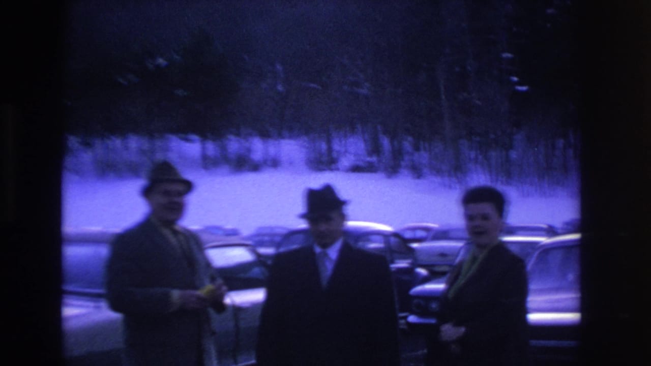 Three men in mid-1960s suits and fedora hats talk in a snow-covered parking lot, Hoboken NJ area, ca. 1966; strong purple-blue cast on aged 8mm stock.