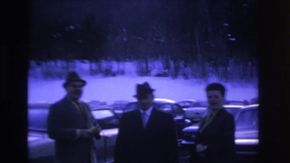 Three men in mid-1960s suits and fedora hats talk in a snow-covered parking lot, Hoboken NJ area, ca. 1966; strong purple-blue cast on aged 8mm stock.