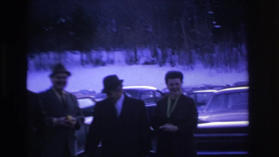 Three men in dark suits and fedoras in a snow-covered parking lot, Hoboken NJ, 1966; blue-purple color cast from aged 8mm film.