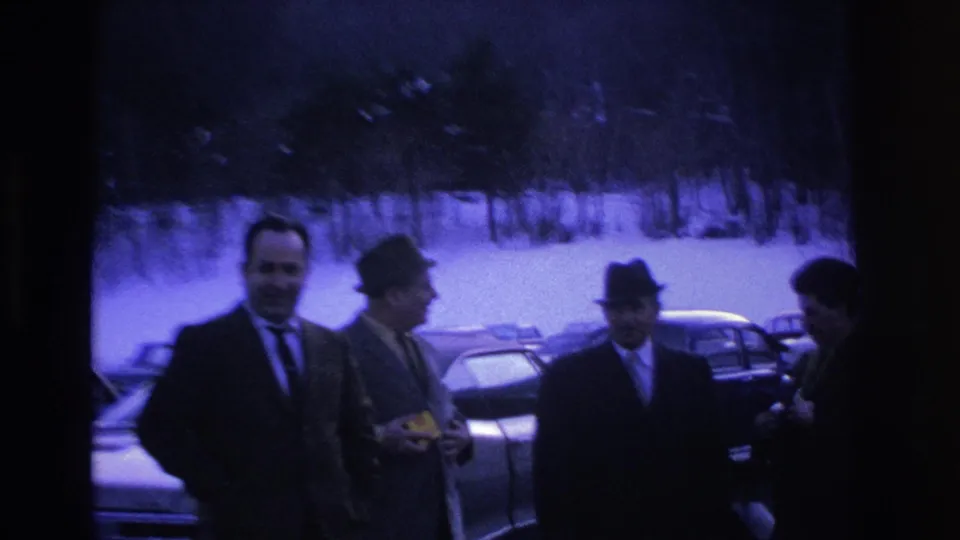 Men in suits and fedoras in a snowy parking lot, Hoboken NJ, c.1966; one man holds a small object; blue-purple dye-decay cast visible on 8mm.