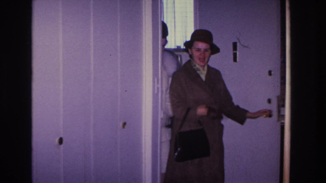 Woman in mid-1960s brown coat and hat turns the doorknob at an interior door in a lavender-walled home; Hoboken, New Jersey, 1966 home movie.