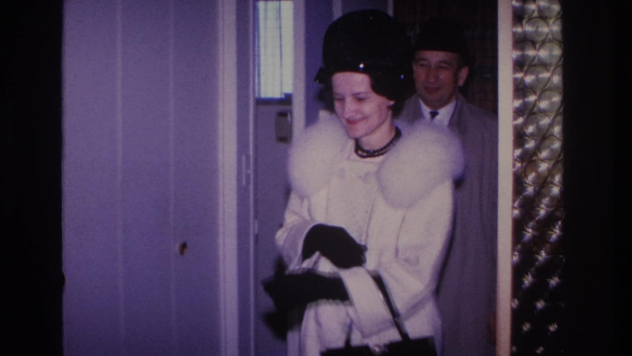 Smiling woman in white fur-collared coat and black hat arriving at a residential doorway, Hoboken New Jersey, circa 1966, 8mm home movie.