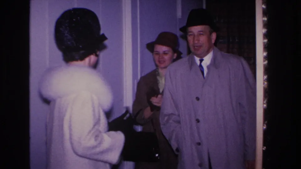 Smiling man in tan overcoat and dark fedora with two women entering a residential hallway, Hoboken New Jersey, circa 1966, 8mm home movie.