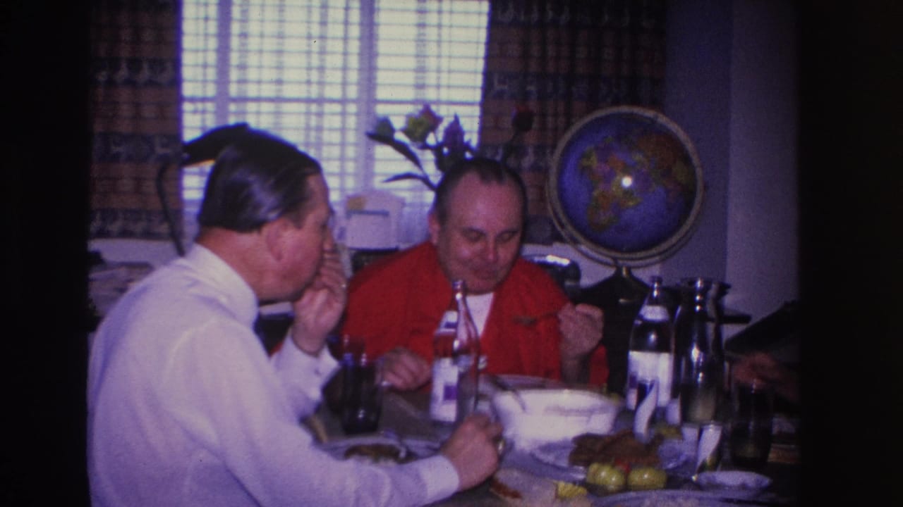 Two adult men sharing a meal at a home dinner table, Hoboken New Jersey, circa 1966; decorative globe and patterned curtains in background.