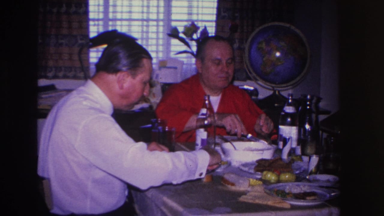 Two men continue their meal at a home dining table, with a decorative globe and horizontal window blinds behind them, circa 1966.