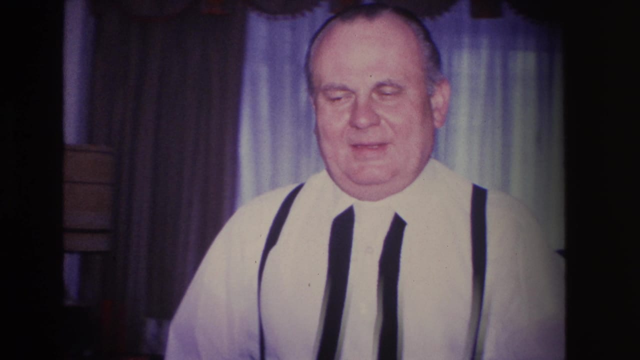 Mid-1960s 8mm home movie close-up: older man in white shirt and dark suspenders, likely at a domestic gathering in Hoboken, New Jersey, circa 1966.