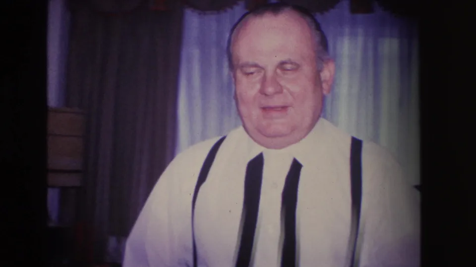Mid-1960s 8mm home movie close-up: older man in white shirt and dark suspenders, likely at a domestic gathering in Hoboken, New Jersey, circa 1966.