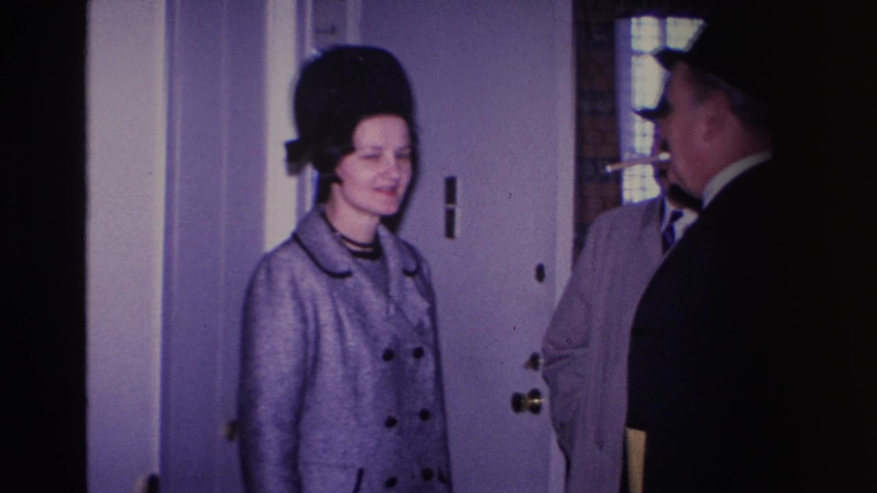 1966 home movie: woman in grey double-breasted coat and tall black hat at a residential doorway, man in dark suit at frame edge, Hoboken, New Jersey.