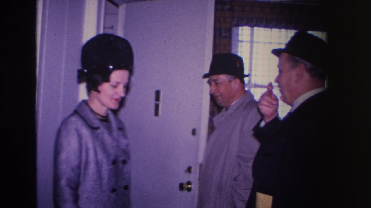 8mm home movie frame from 1966 Hoboken, New Jersey — woman in structured black hat and two men in suits and fedoras near a white interior door; one man holds what appears to be a cigarette.