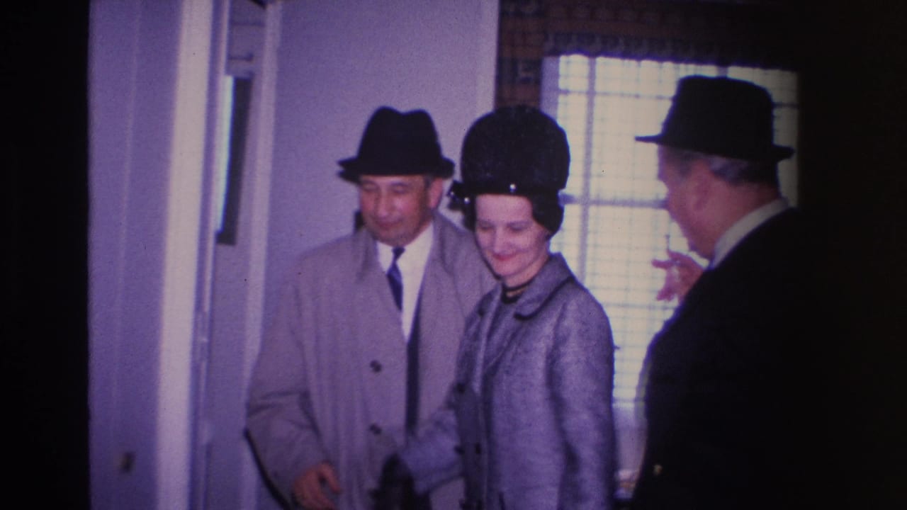 Three adults in mid-1960s dress entering a residential hallway in what is described as Hoboken, New Jersey, 1966; the woman wears a gray coat and black pillbox hat and is smiling.