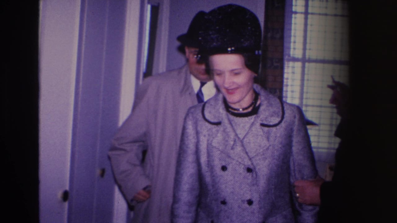 Close view of a smiling woman in a gray double-breasted textured coat with black trim and black hat entering a doorway in what is described as a Hoboken, New Jersey home, 1966.