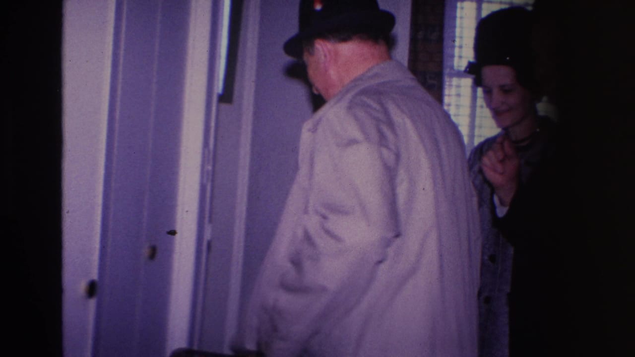 Man in tan trench coat and dark fedora arriving at a home entrance, greeted by a woman in a dark coat and hat — Hoboken, New Jersey, circa 1966.