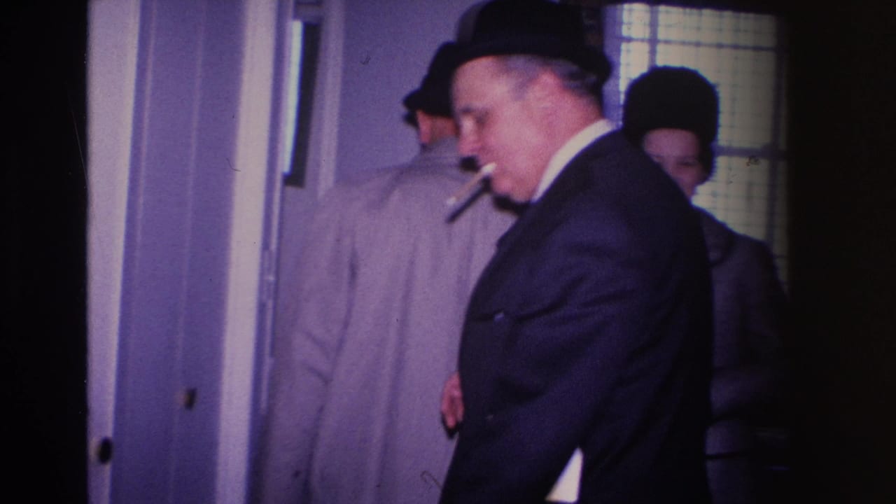 Man in tan overcoat with cigarette, partially turned at a home doorway, other guests visible in background — domestic interior, Hoboken, New Jersey, circa 1966.