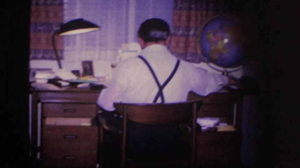 8mm home movie frame circa 1966 showing a man at a home-office desk with a globe and lamp, Hoboken, New Jersey.