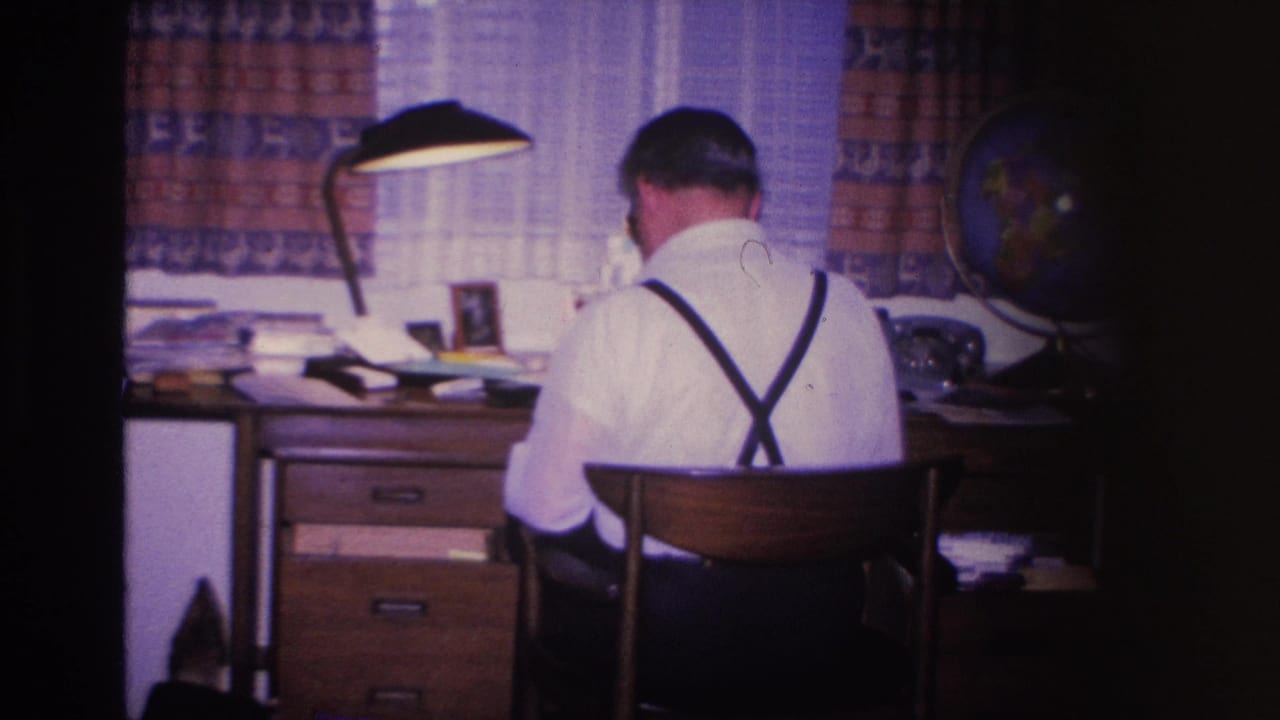 Sustained shot of man in suspenders at mid-century wooden desk; lamp and globe in background; 8mm home movie, Hoboken, New Jersey, circa 1966.