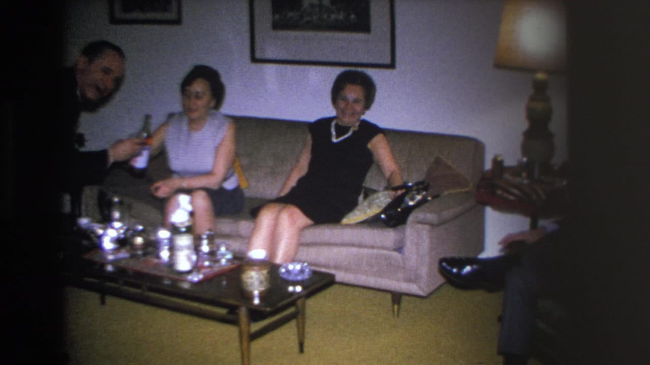Two women on a mid-century sofa in a 1966 Hoboken home; one in a dark dress with pearl necklace, the other in a sleeveless top; drinks on coffee table.
