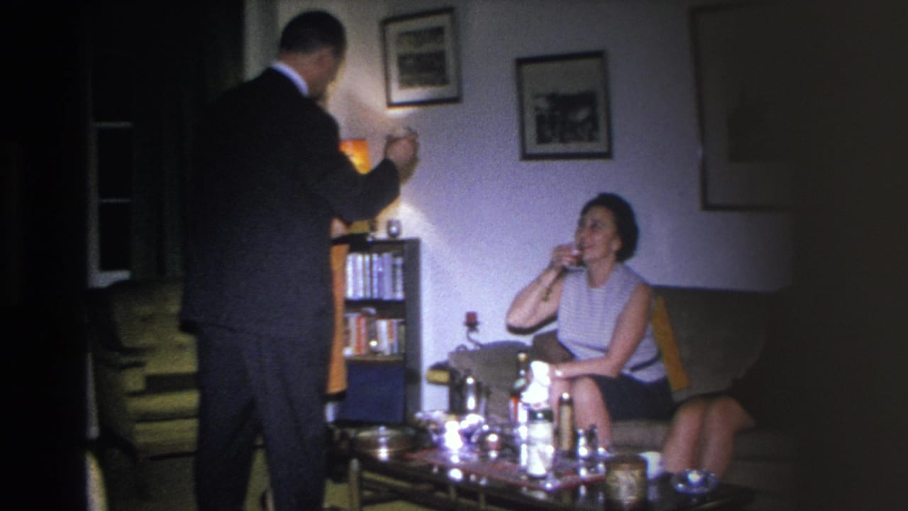 8mm home movie c.1966, Hoboken NJ; man in dark suit standing at left, woman in sleeveless dress seated sipping a drink, mid-century coffee table with bottles in foreground.