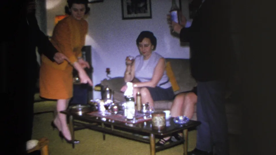 1966 Hoboken home movie: two women at a mid-century living room party, coffee table laden with bottles and glasses.