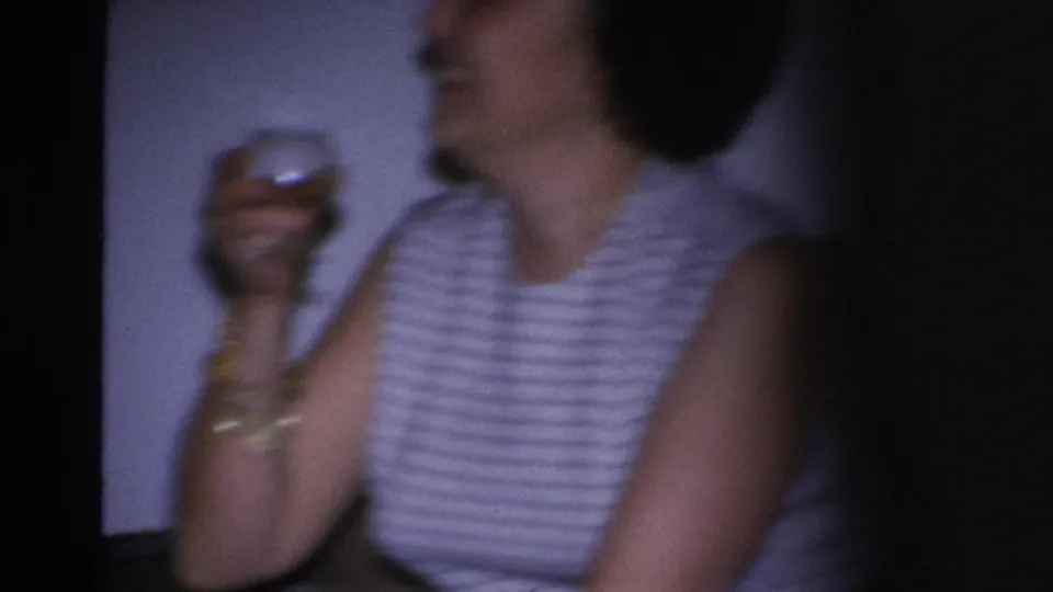 Extreme close-up 8mm frame of a woman in a 1960s striped sleeveless top holding a glass; gold bracelet visible, face cropped at top of frame.