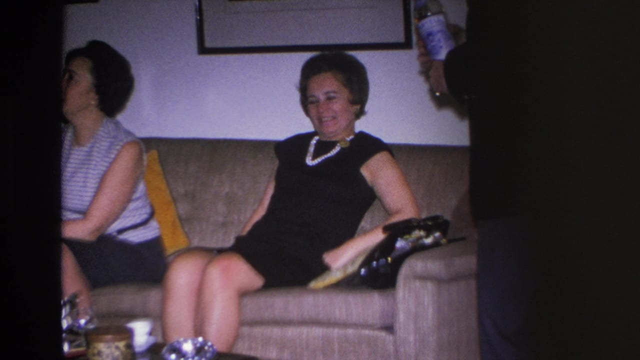 Two women on a tan sofa in a mid-1960s Hoboken living room as a man's hand holds a Martini vermouth bottle into frame, circa 1966.