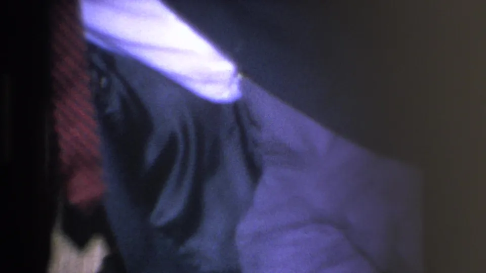 Blurred close-up of a man's dark suit and patterned tie at a mid-1960s home gathering in Hoboken; likely a camera pan or unintended capture at clip end.