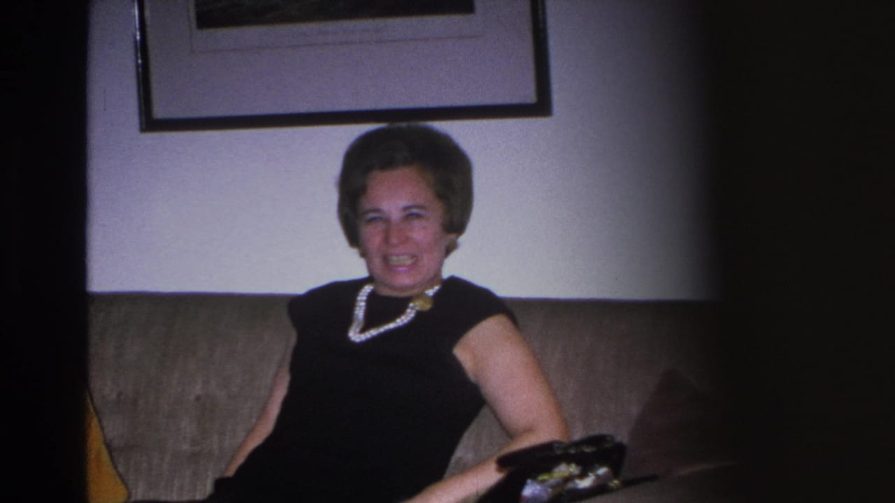 Close-up of a woman in a black dress and pearl necklace laughing on a sofa in a mid-century American living room, circa 1966, Hoboken, NJ.