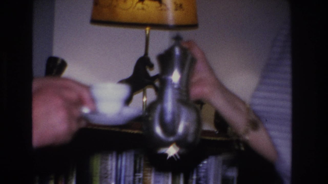 Tea being poured from a silver teapot into a white cup held by a man's hands; bookshelves and horse-illustrated lamp shade visible in background of a 1966 living room.
