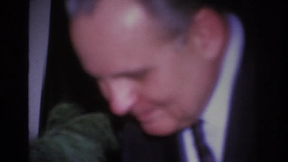 Extreme close-up of a man looking down in a dark suit and tie, candid 8mm moment at a Hoboken social gathering, circa 1966.