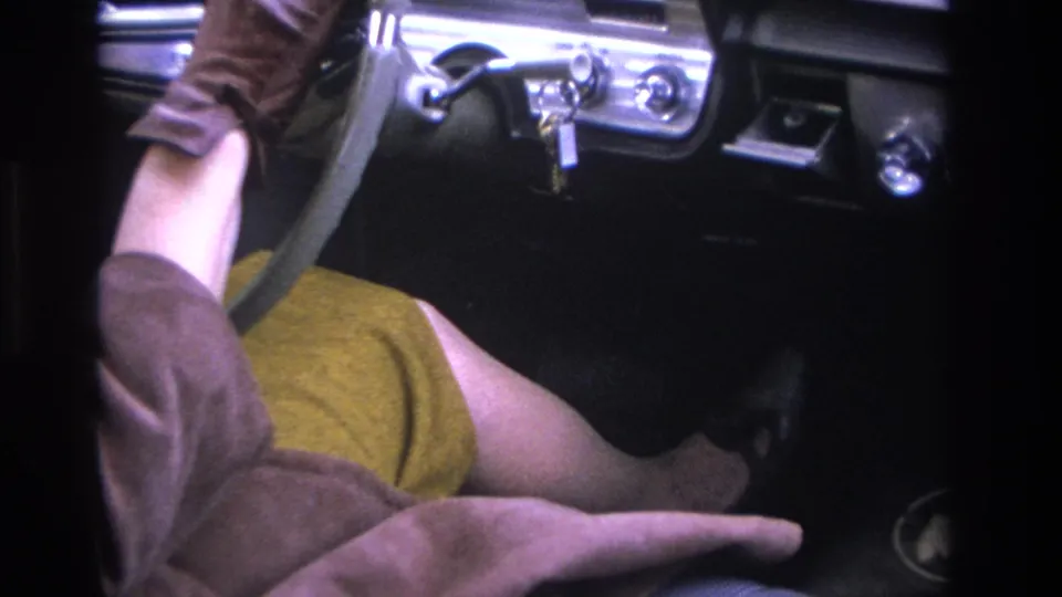Final frame showing a woman in brown coat and mustard skirt in what appears to be a mid-1960s American car, gloved hand extended toward the brake pedal with chrome dashboard trim visible.