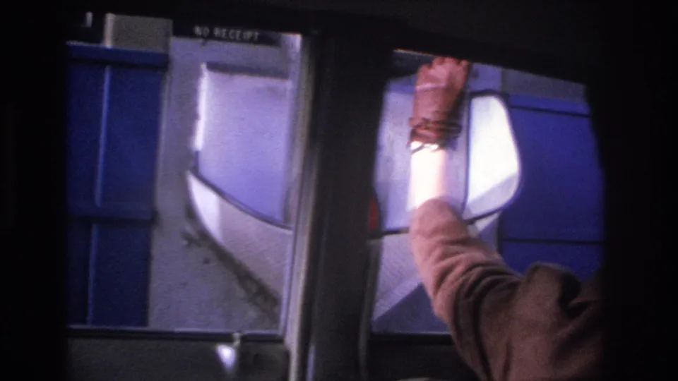 1966 8mm close-up of a woman's outstretched arm depositing coins into a toll booth basket; 'NO RECEIPT' sign visible on the blue booth structure.