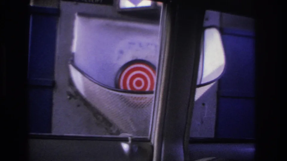 8mm frame showing the interior view of a 1966 New Jersey toll booth with a red-and-white bullseye target sign on the blue-paneled structure.