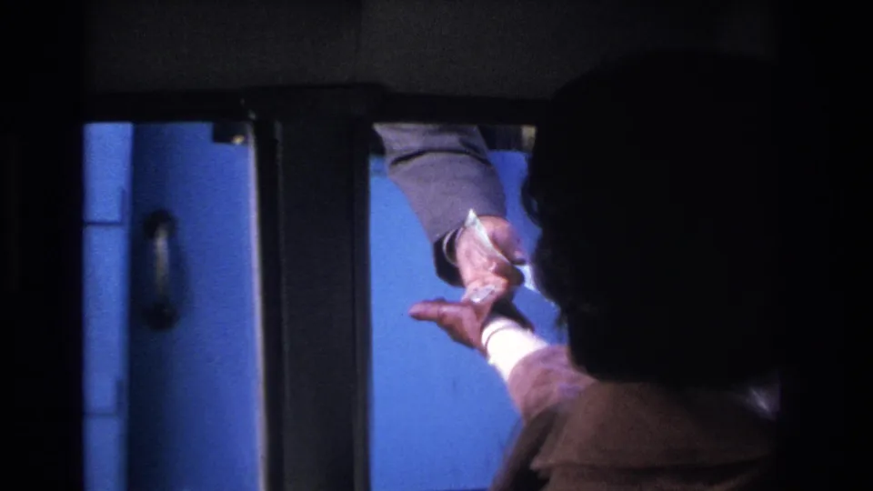 1960s toll payment: gloved driver's hand passes paper currency through car window to an attendant's hand, vivid blue exterior light, 8mm film.