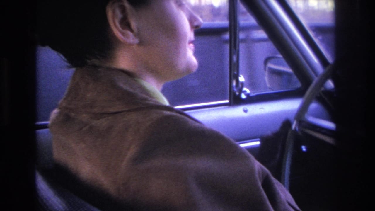 Dark-haired woman in brown coat in close right-facing profile from the passenger seat of a car, Hoboken, New Jersey, circa 1966 home movie.