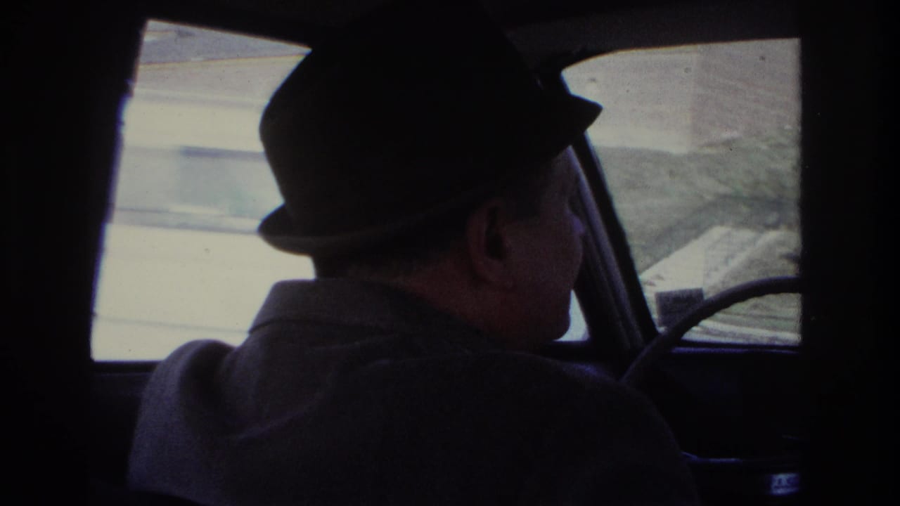 Driver in a dark hat turns his head slightly inside a car.