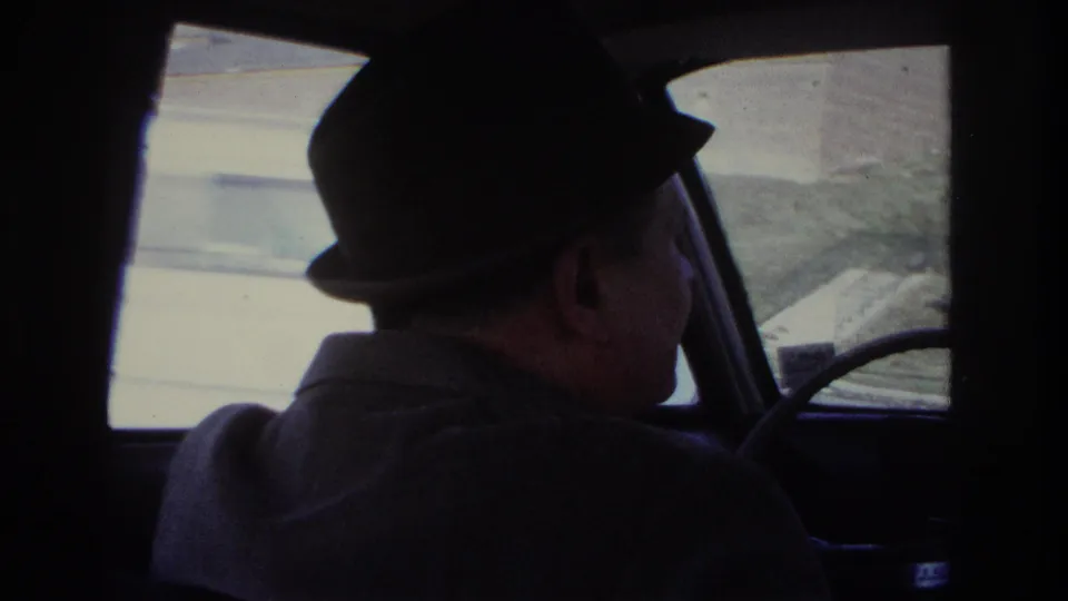 1966 Hoboken car interior with the fedora-wearing driver in profile and the steering wheel visible near the windshield.