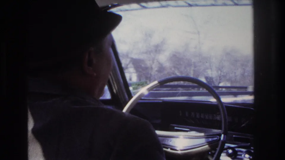 Shadowed 1966 Hoboken car-interior frame showing the driver in profile beside the steering wheel and windshield view.