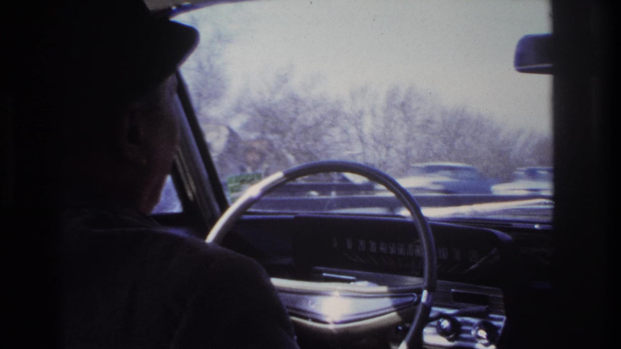 Driver seen from the passenger side inside a moving car with highway traffic ahead.